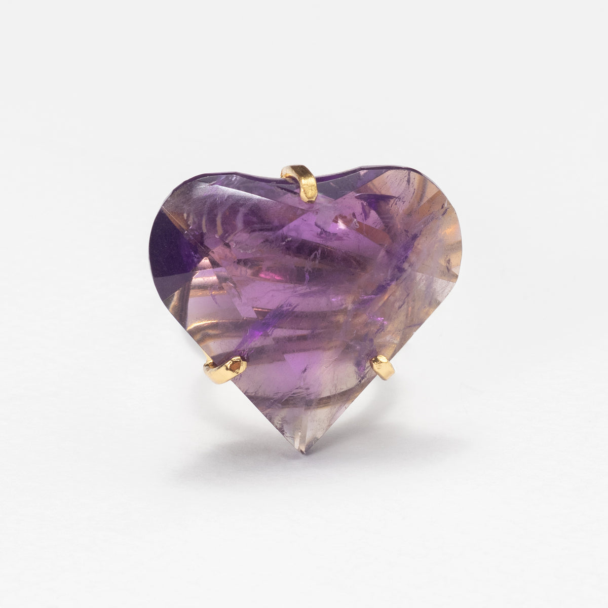 A heart-shaped purple gemstone ring with gold prongs, set against a plain white background.