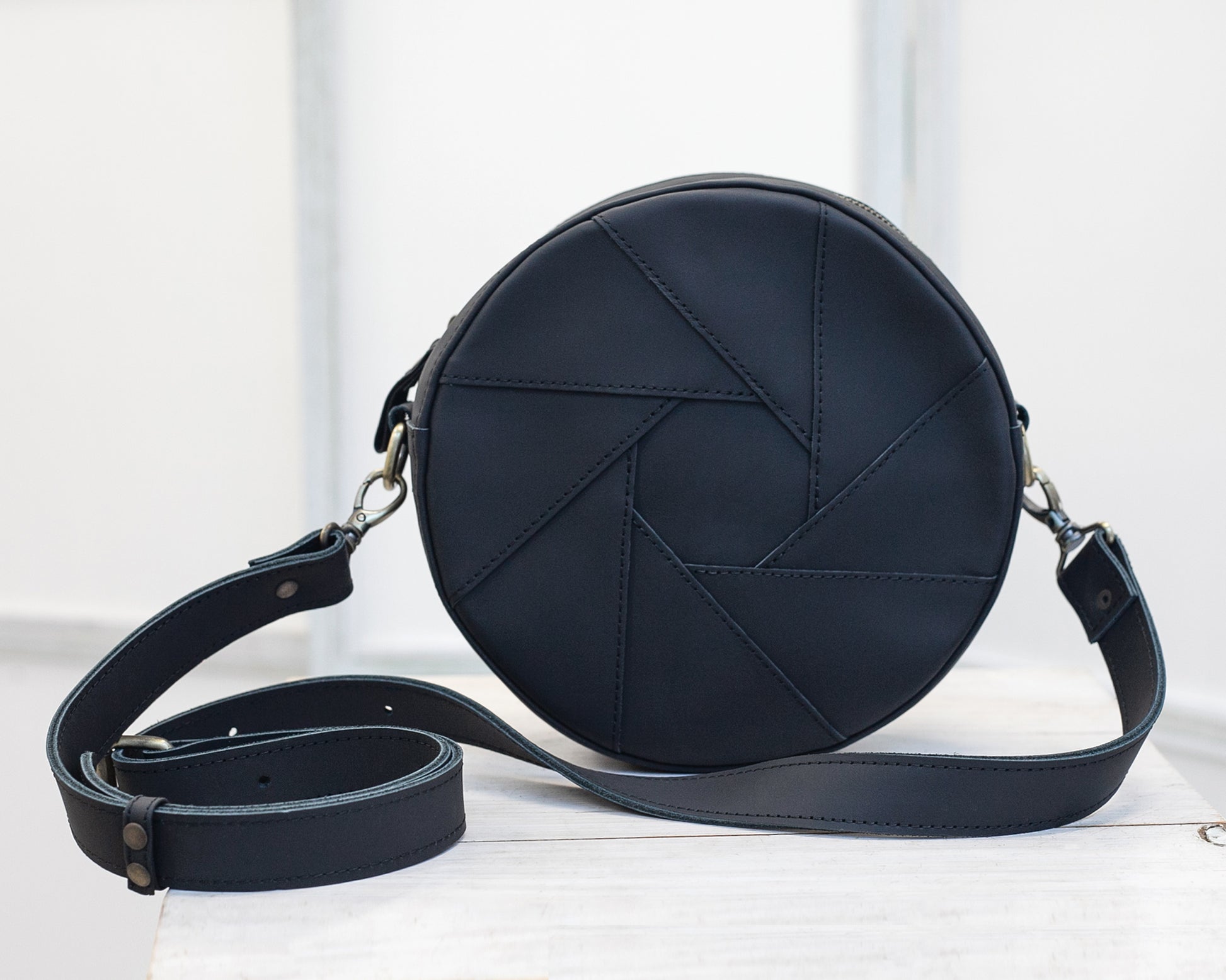 The back side of a black round crossbody bag on a white background.