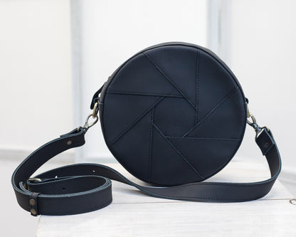 The back side of a black round crossbody bag on a white background.