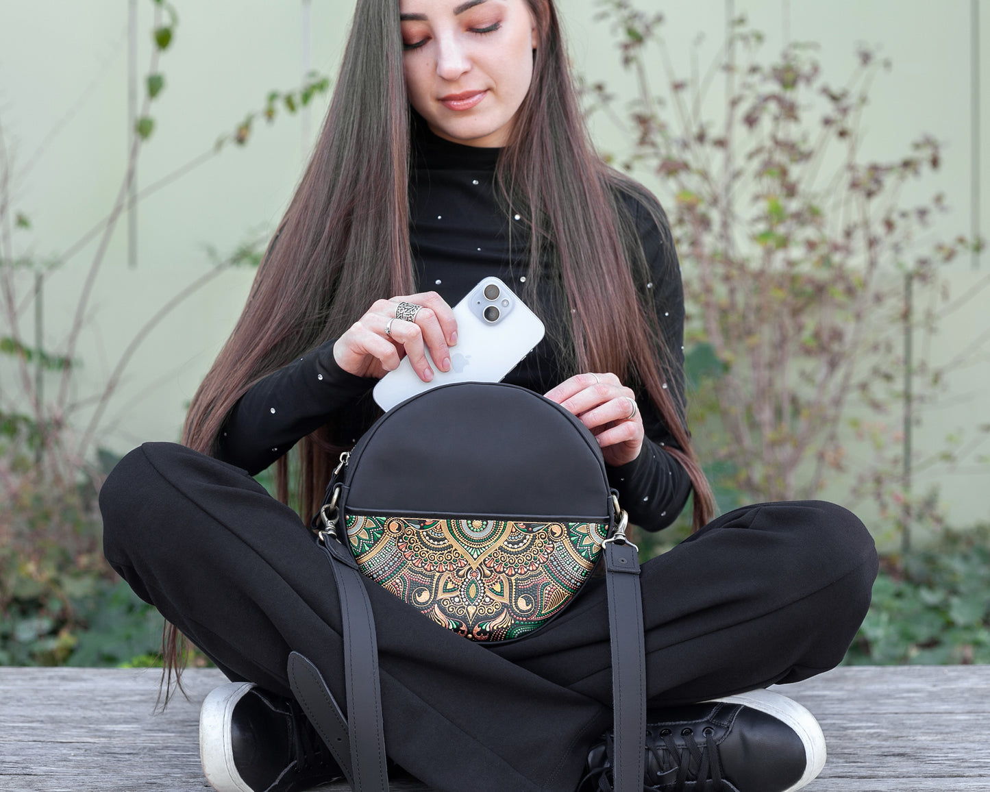 Woman sitting on a bench holding a black bag with a colorful pattern.