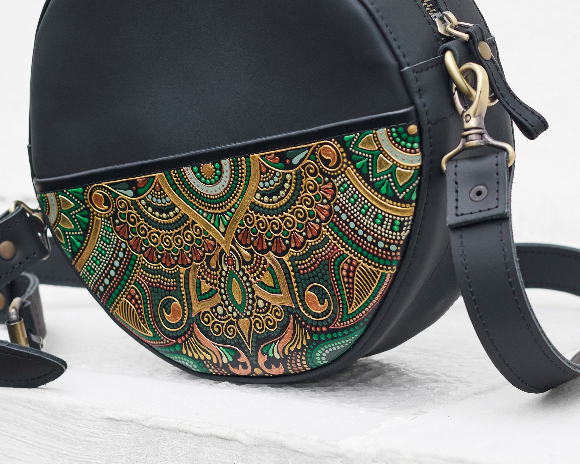 Black handbag with a colorful green floral pattern on a light wooden surface