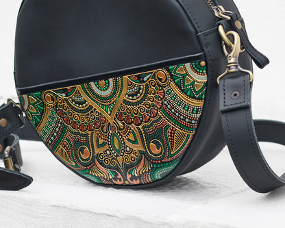 Black handbag with a colorful green floral pattern on a light wooden surface