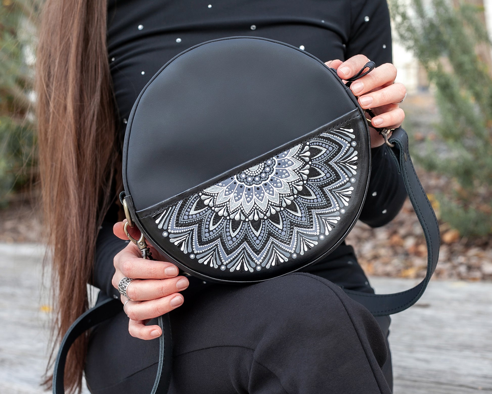 Person holding a black round bag with a white mandala design outdoors.