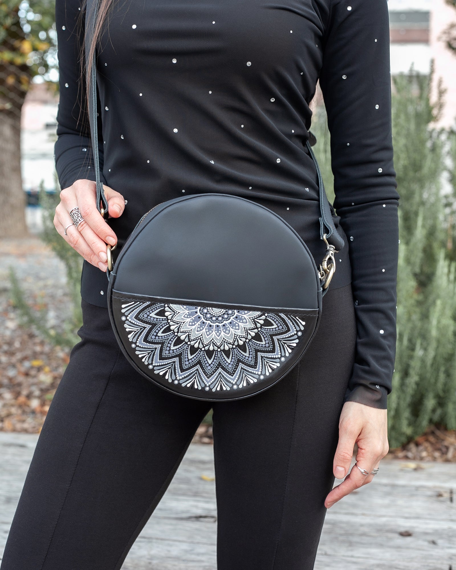 Woman in a black long-sleeve top and pants wearing a black round crossbody bag with a white pattern.