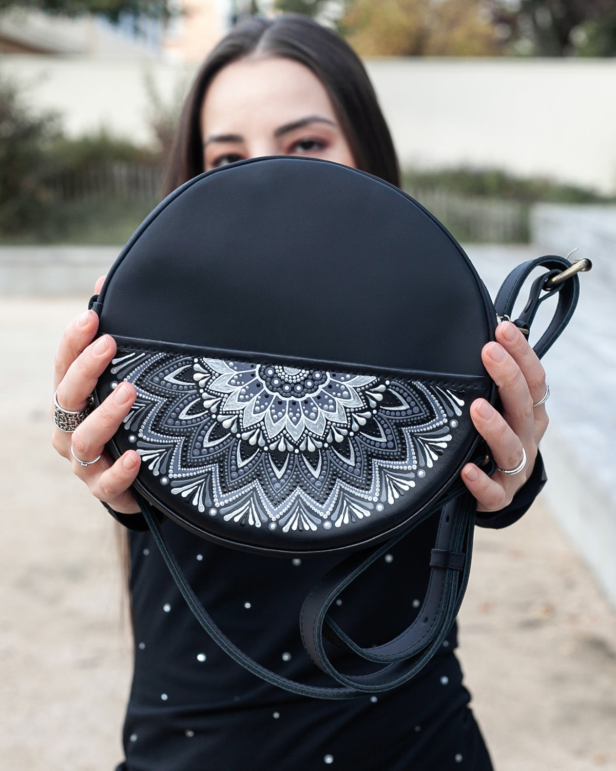 Woman showing a black round bag with a white mandala design.