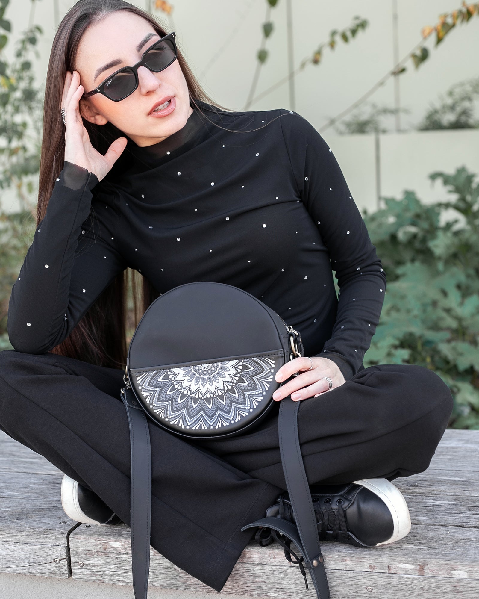 Woman holding a black round bag with a white pattern, wearing sunglasses and a black outfit.