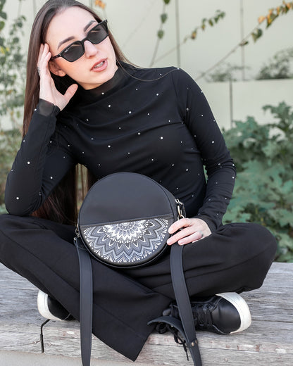 Woman holding a black round bag with a white pattern, wearing sunglasses and a black outfit.