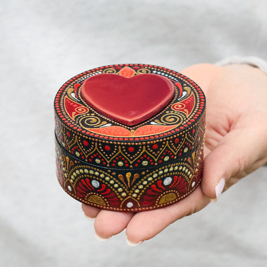 Decorative heart-shaped box with intricate patterns held in a hand against a neutral background