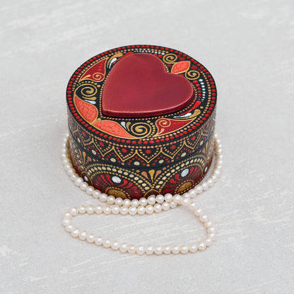 Decorative heart-shaped box with intricate patterns and a pearl necklace on a light gray background