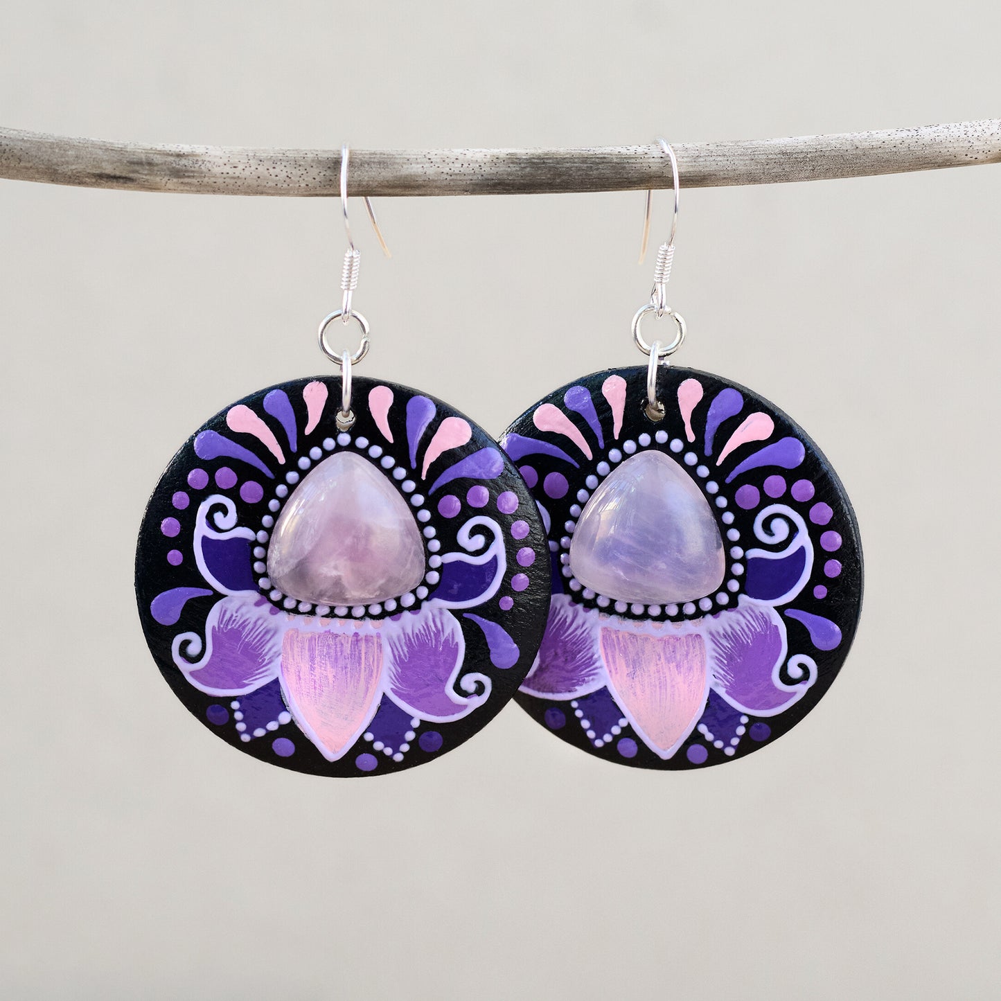 Wooden earrings with purple and pink floral design and rose quartz cabochon on a gray background