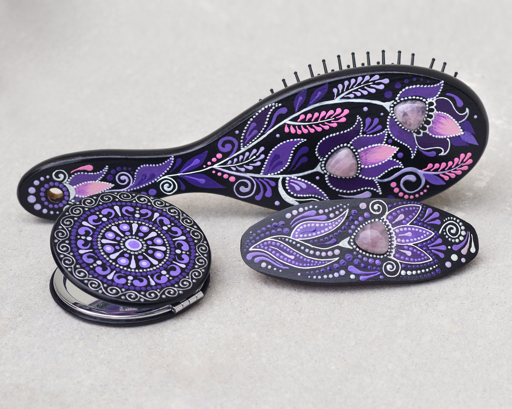 Purple hairbrush, mirror and barrette with purple and pink floral patterns on a light gray background