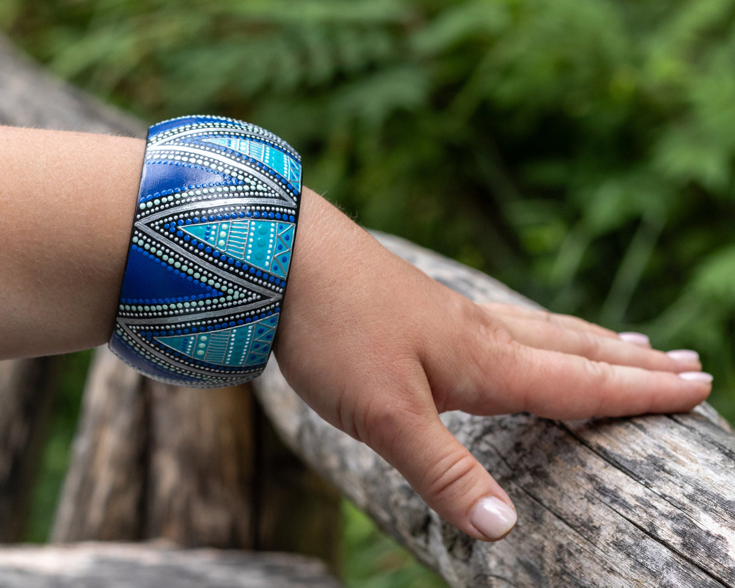 Hand wearing a blue patterned bracelet against a natural background