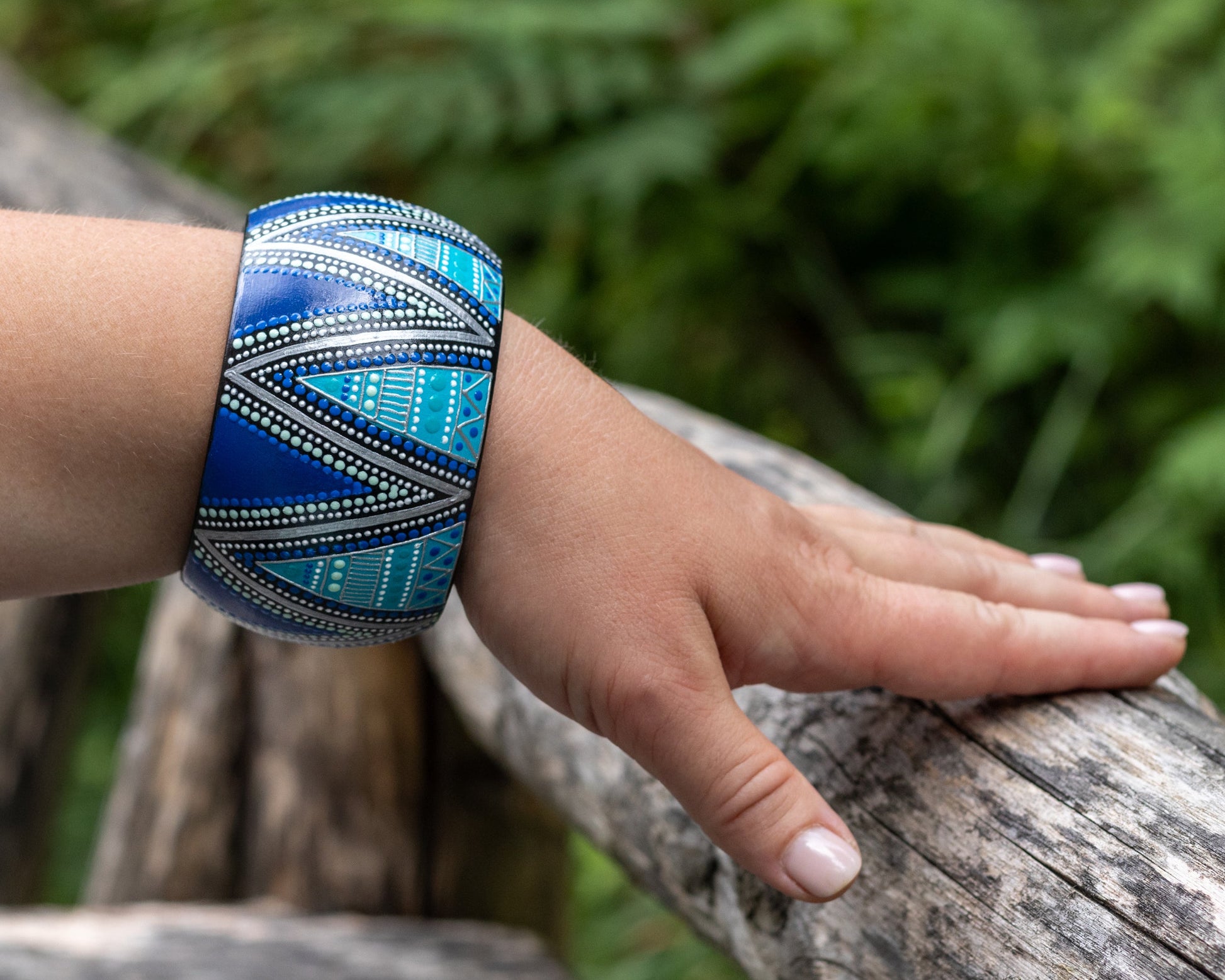 Hand wearing a blue patterned bracelet against a natural background