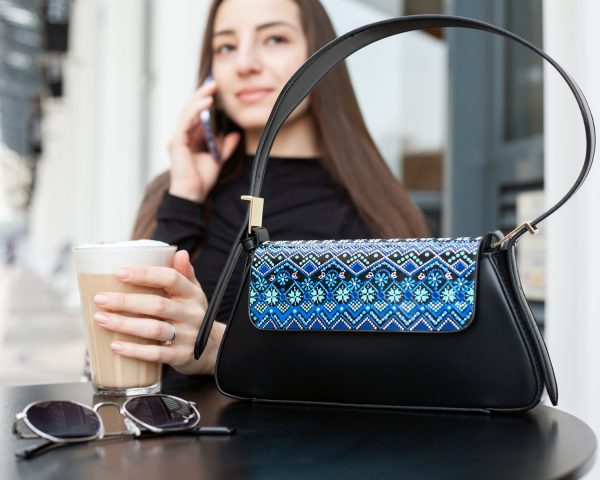 Woman sitting at the cafe having a coffee. Small black bag with hand-painted blue design standing on the table in the foreground