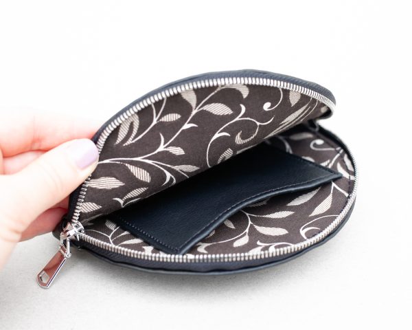 Close-up view of the hand opening wallet with brown floral cotton lining inside and a small leather pocket.